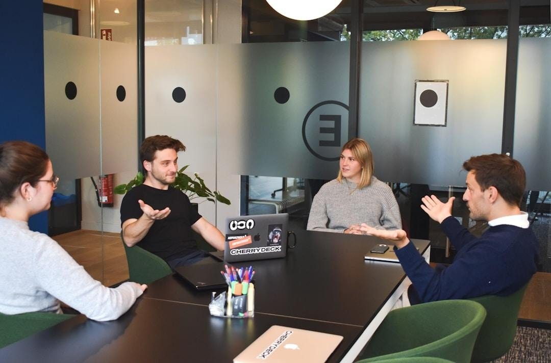 Four individuals collaborating on proposal management tools while sitting around a table in an office space.